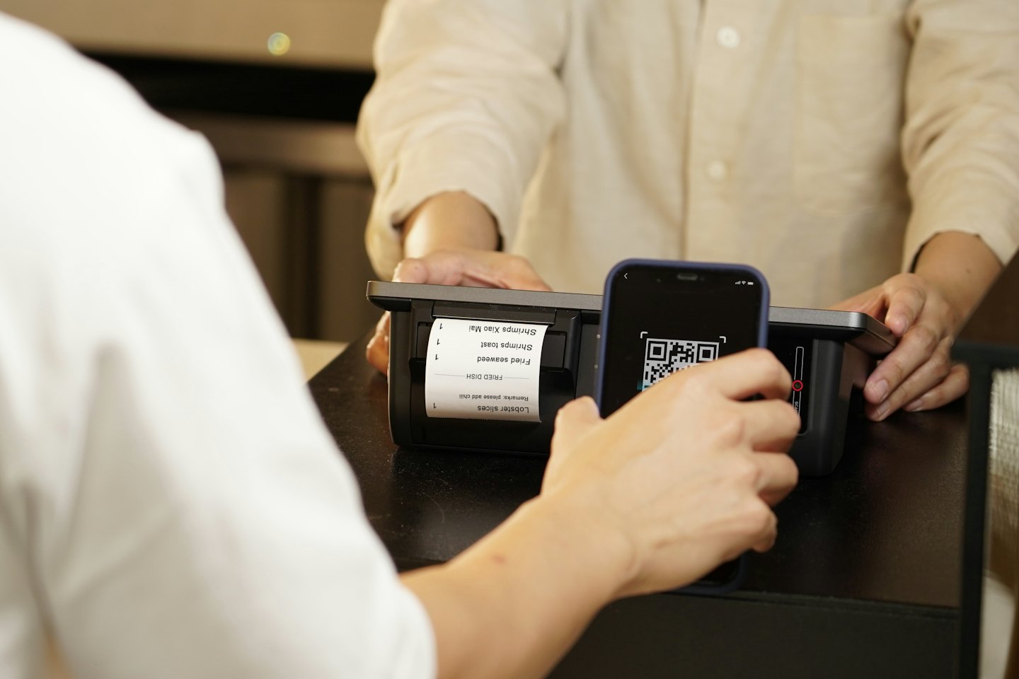 Customer scanning a smartphone QR code at a payment terminal.