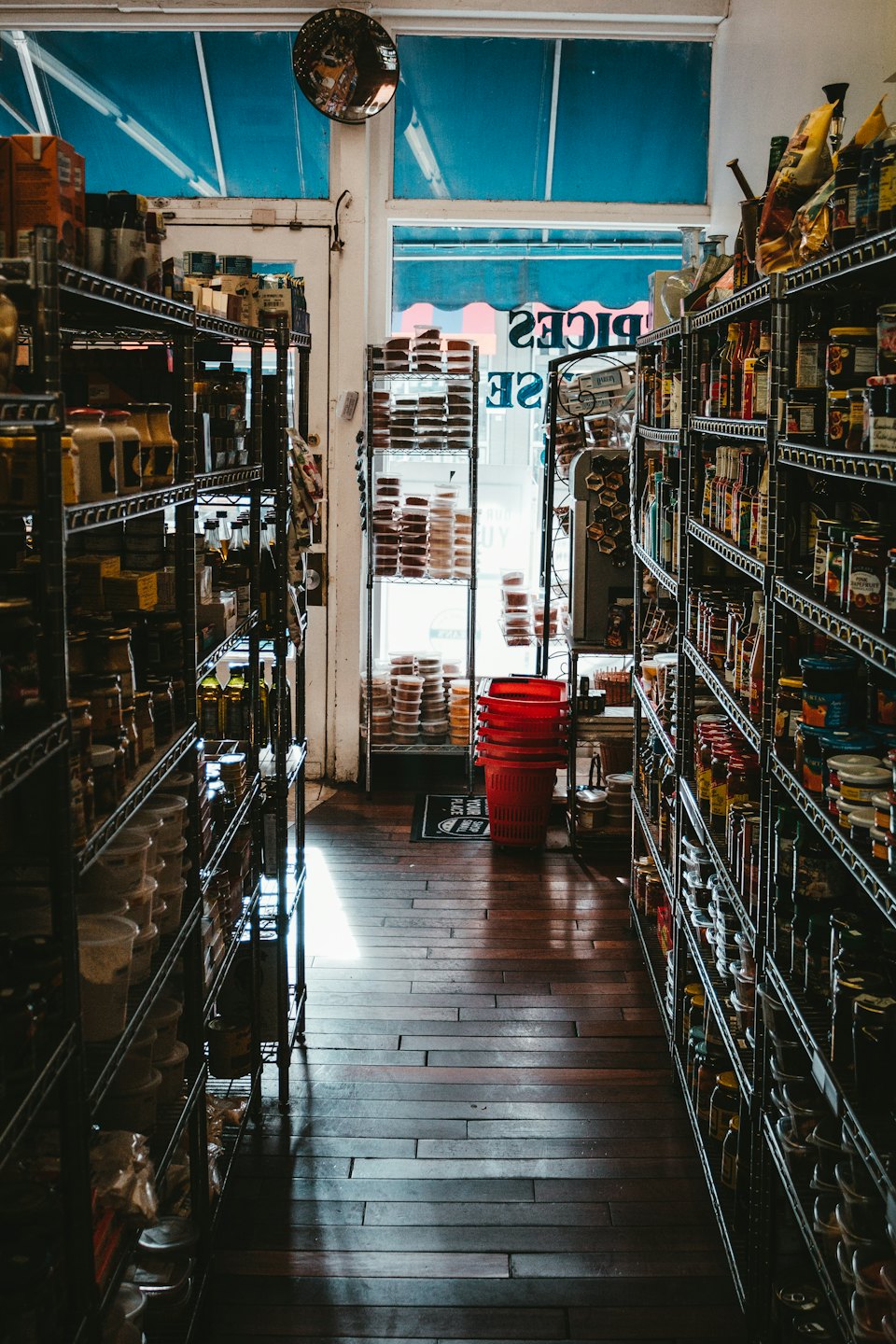 Narrow grocery store aisle filled with products leading to a bright entrance.